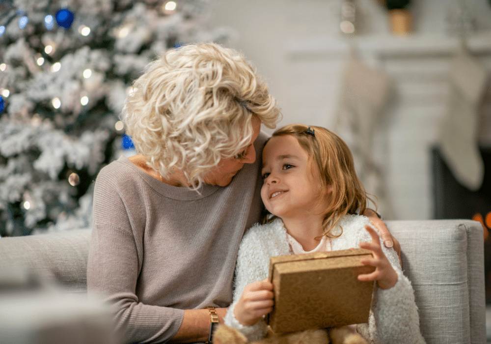 Grandparent giving a wrapped STEMKids science and engineering gift box to their grandchild, smiling together at home during Christmas. STEM Gifts.